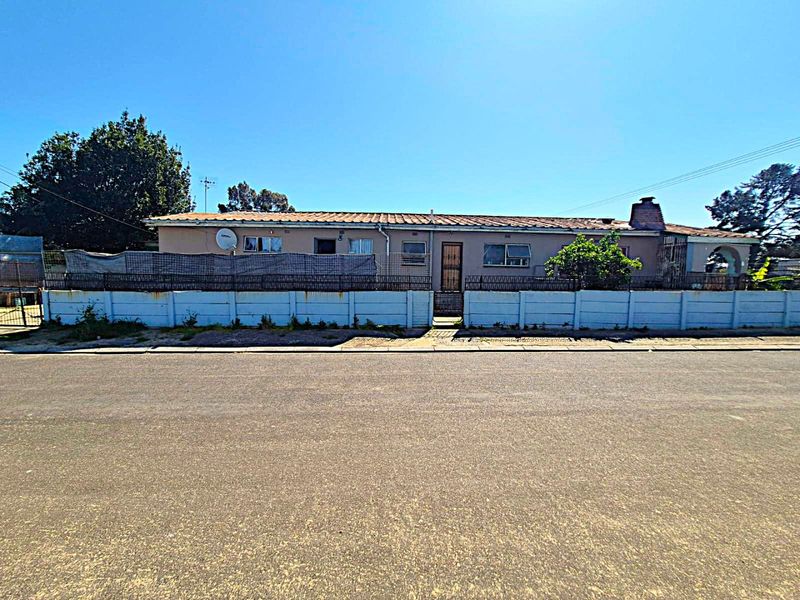 Front view of a single-story residential property featuring a tiled roof, brick chimney, and a concrete boundary wall with metal security fencing.