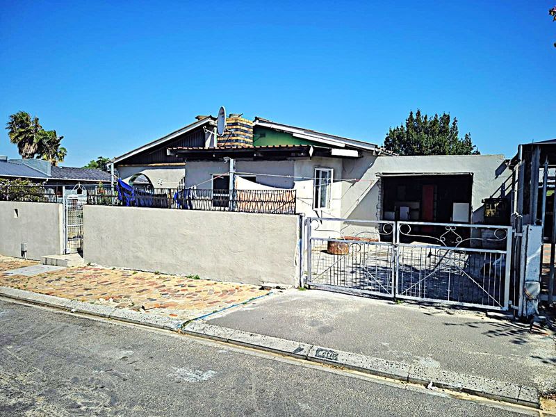 Front exterior view of a single-story house featuring a perimeter wall, metal driveway gate, and paved entrance area.