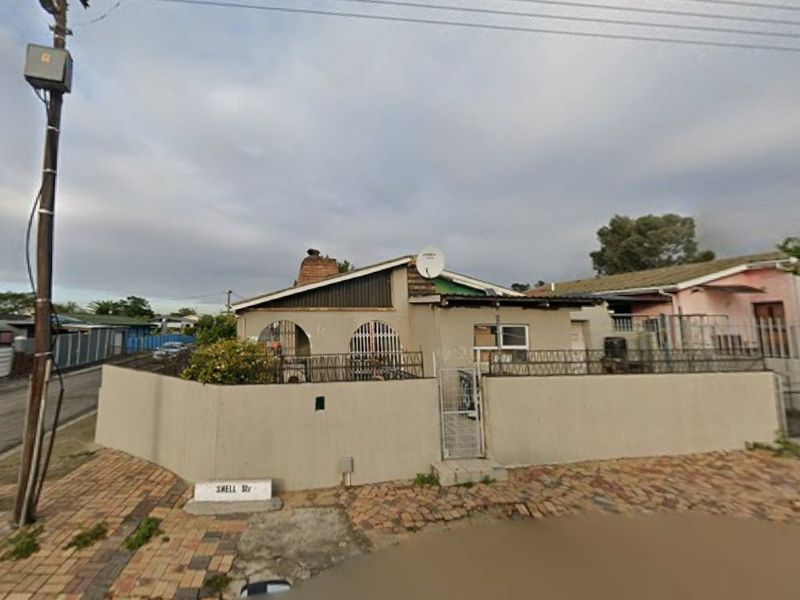 Front exterior view of a single-story house featuring a perimeter wall, security gate, and brick chimney, situated on a corner street plot.
