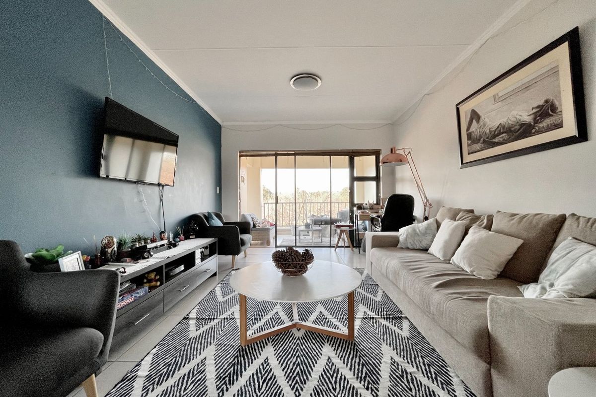A well-lit living room featuring an accent wall, tiled flooring, and large sliding glass doors providing access to an outdoor balcony area.