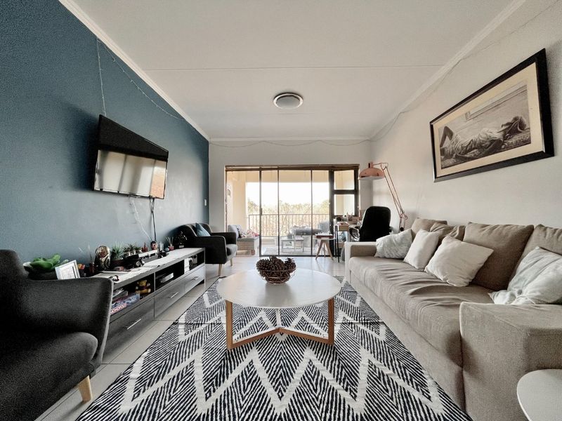 A well-lit living room featuring an accent wall, tiled flooring, and large sliding glass doors providing access to an outdoor balcony area.
