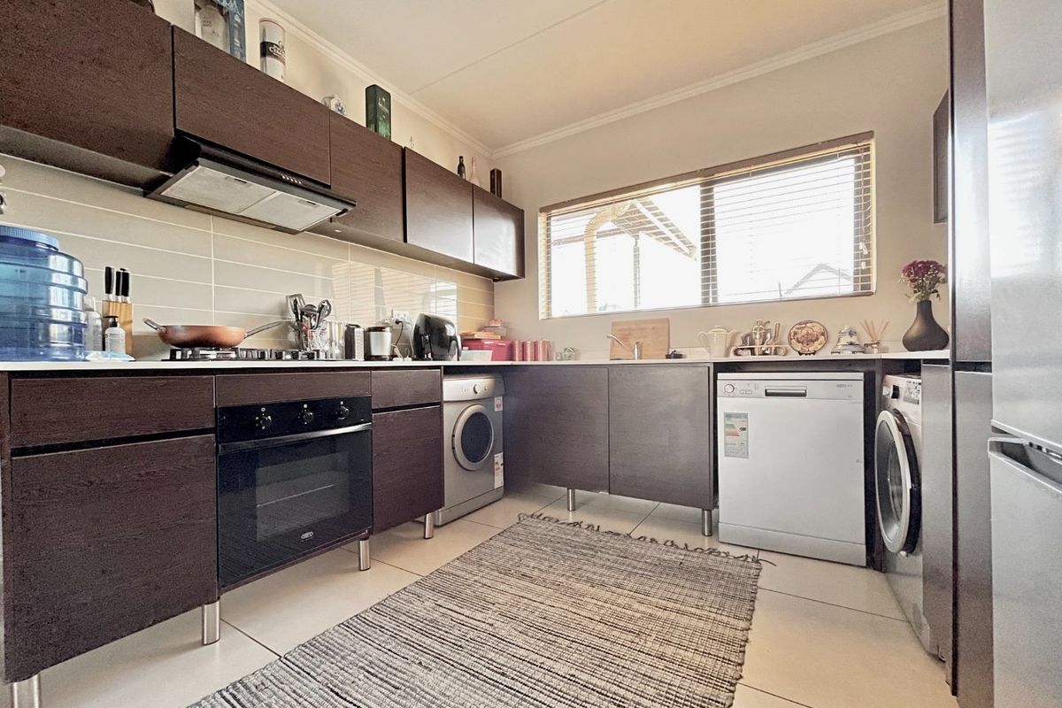 A functional kitchen featuring dark wood cabinetry, built-in oven and hob, tiled backsplash, and integrated space for laundry appliances.