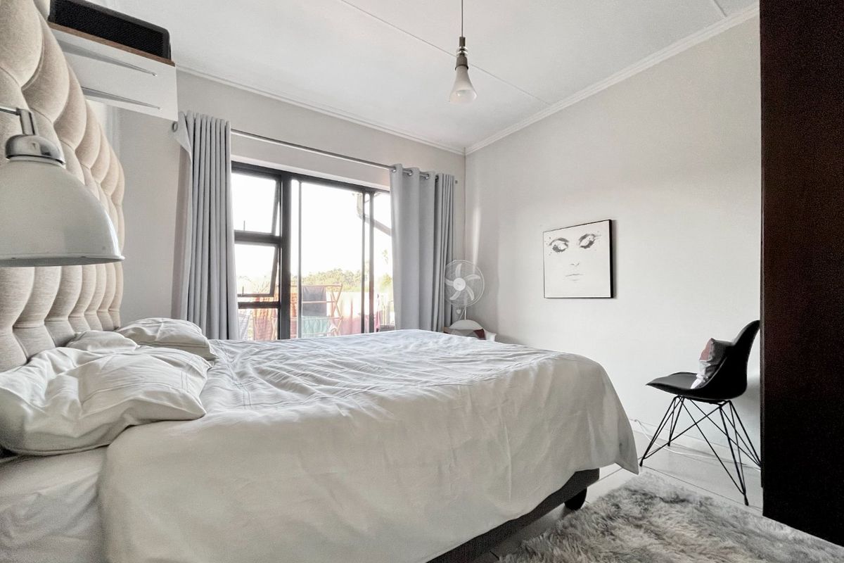 A well-lit bedroom featuring neutral walls, a coved ceiling, and an aluminium sliding door providing access to the exterior.