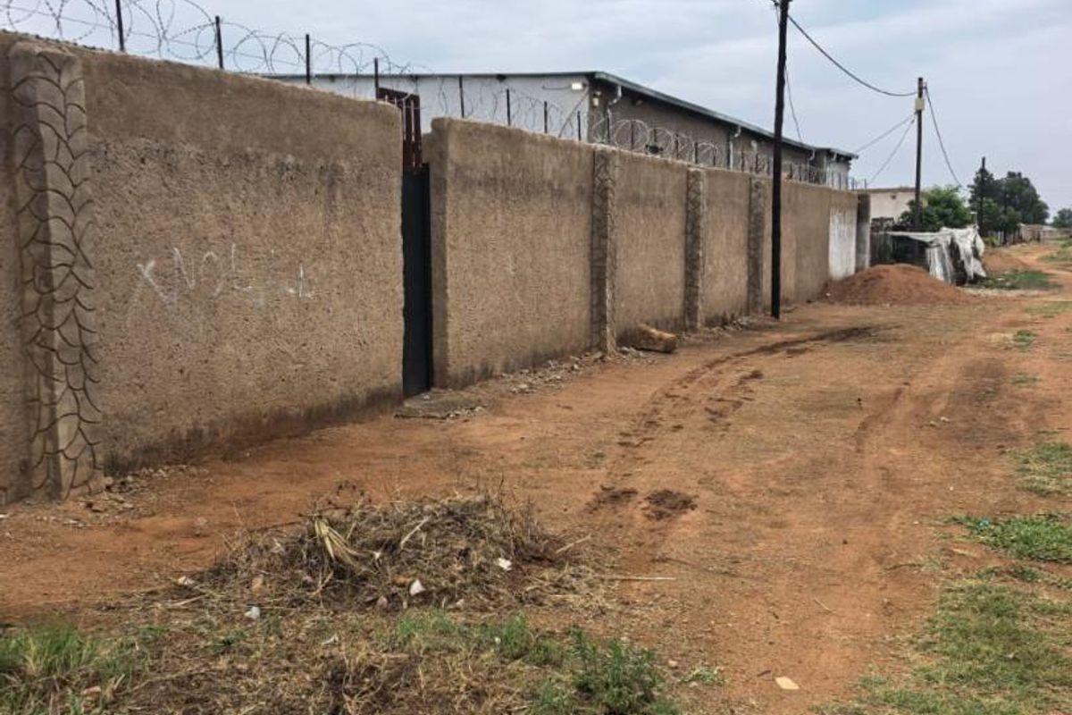 Exterior view of a commercial property featuring a high perimeter wall with razor wire security and a metal access gate.