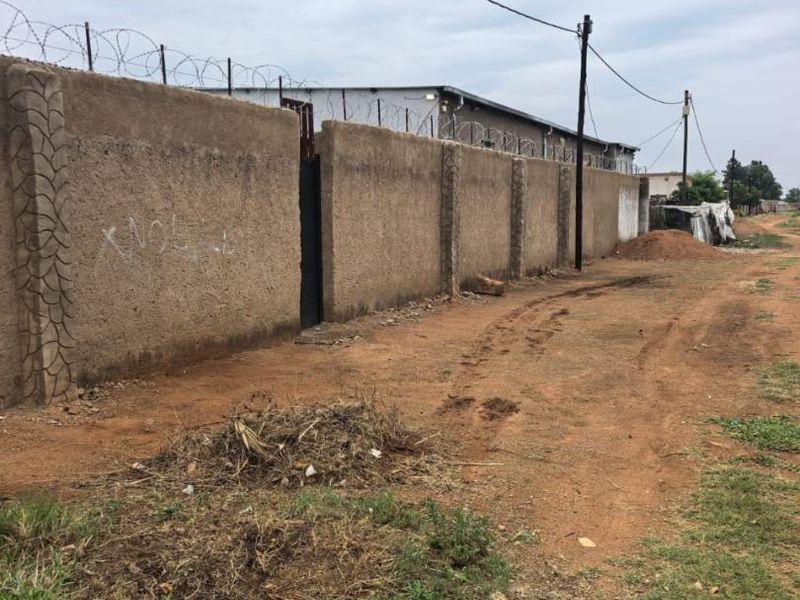 Exterior view of a commercial property featuring a high perimeter wall with razor wire security and a metal access gate.