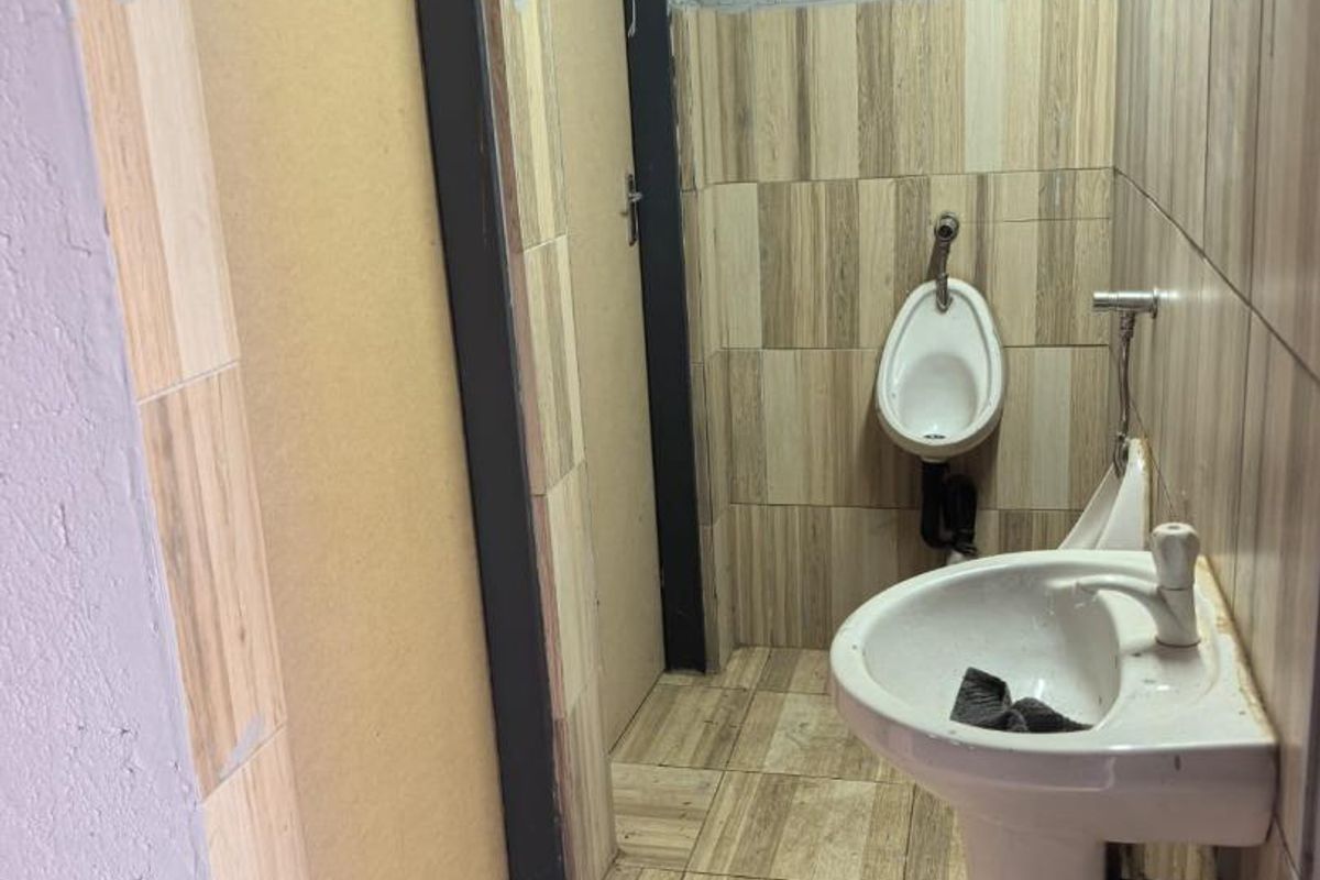 A commercial bathroom facility featuring a pedestal sink and urinal with tiled surfaces, currently requiring maintenance and finishing of walls and ceiling.