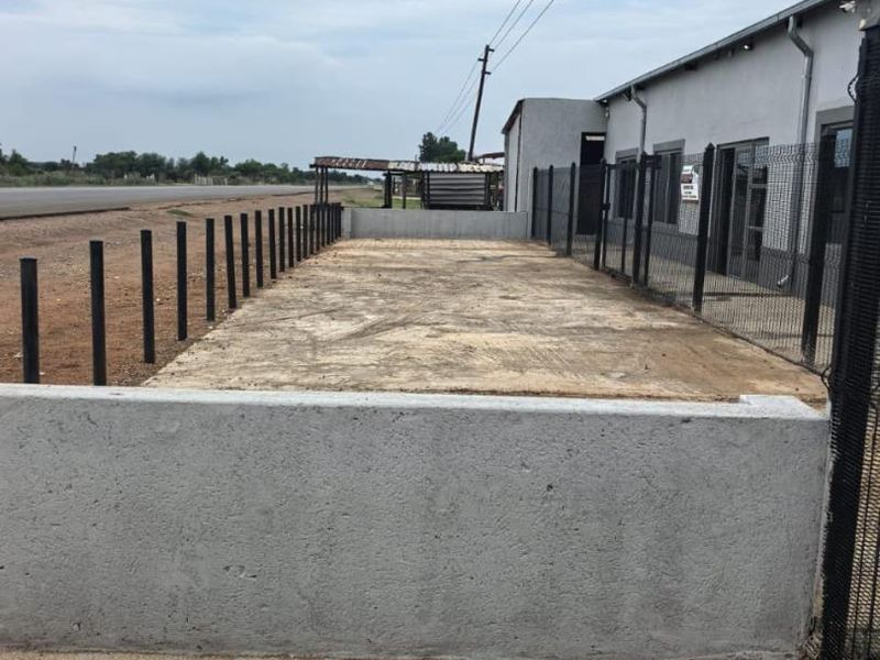 An outdoor commercial area featuring a concrete slab, perimeter mesh fencing, and a low concrete retaining wall adjacent to the building.