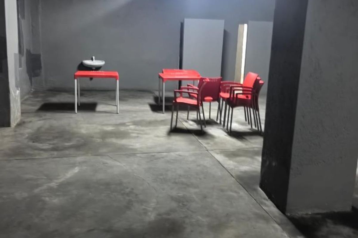 A utilitarian commercial space featuring concrete flooring, a wall-mounted basin, and structural columns, suitable for various business or storage applications.