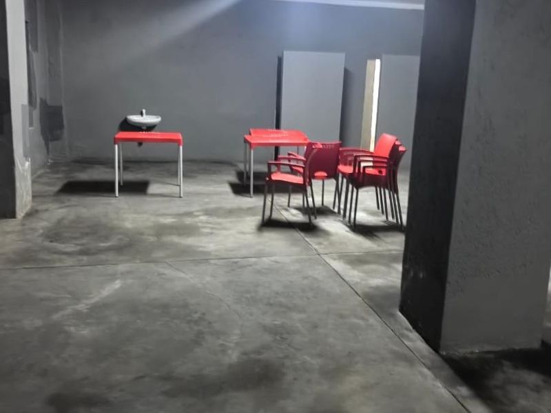 A utilitarian commercial space featuring concrete flooring, a wall-mounted basin, and structural columns, suitable for various business or storage applications.