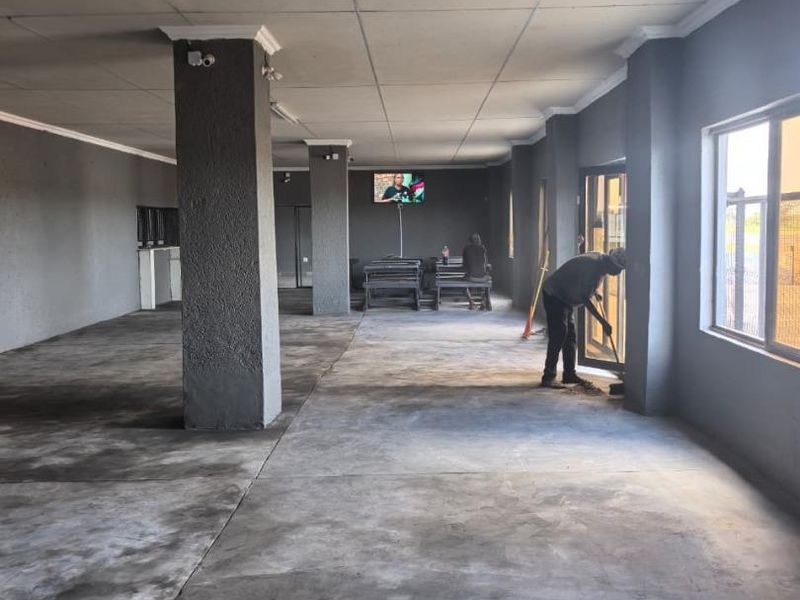 Spacious open-plan commercial area featuring concrete flooring, structural columns, and large windows, currently in a shell-like condition suitable for various business fit-outs.