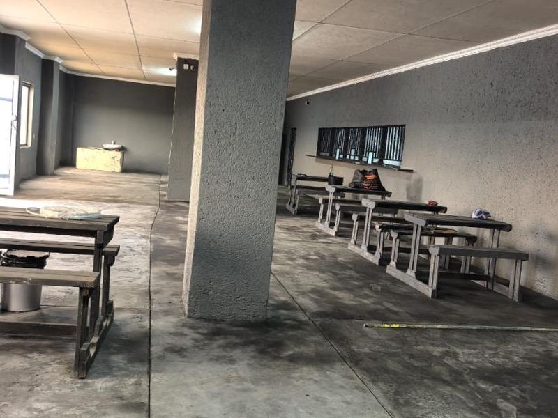 A covered outdoor commercial patio area featuring concrete flooring, structural columns, and security-barred windows, suitable for renovation or functional space improvement.