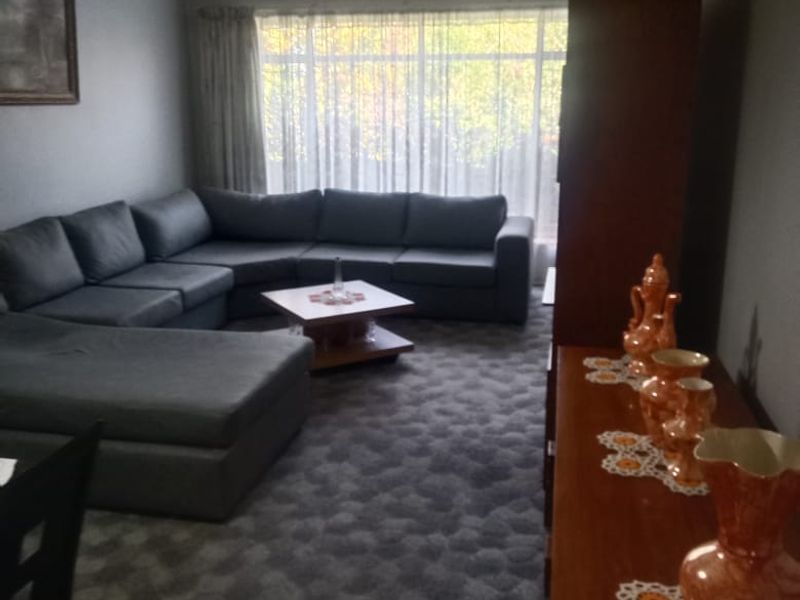A living room featuring carpeted flooring, a ceiling fan, and a large window allowing natural light into the space.
