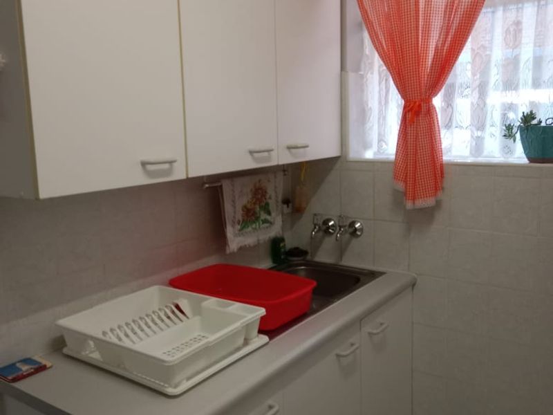 A functional laundry area featuring white built-in cabinetry, a stainless steel sink, and tiled splashbacks.