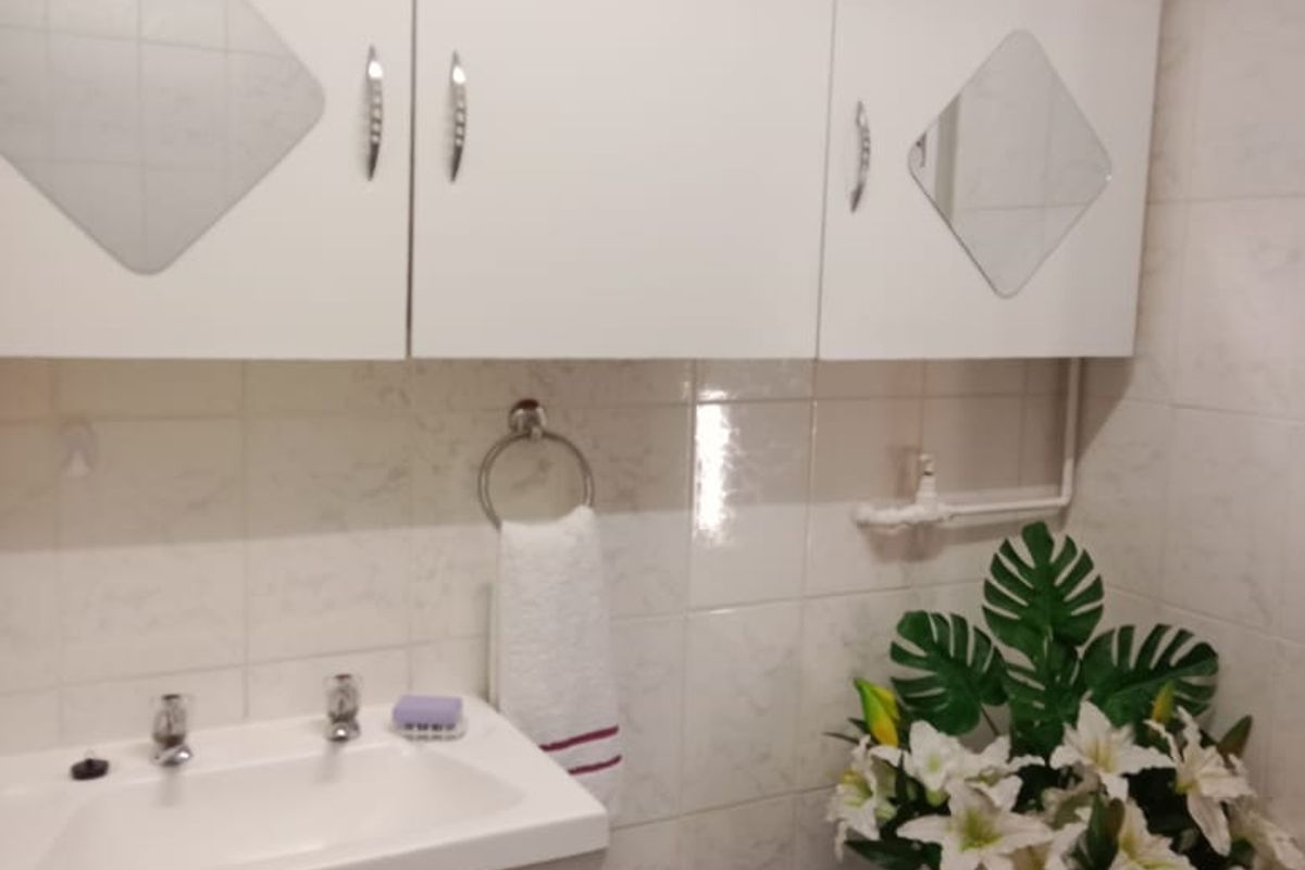 A functional bathroom featuring a vanity cabinet with a ceramic basin, wall-mounted storage units, and tiled finishes throughout.