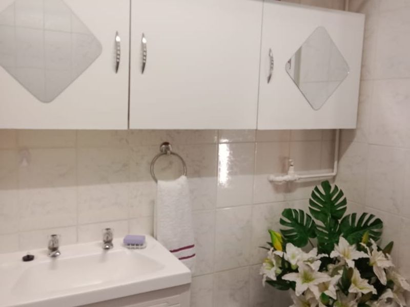 A functional bathroom featuring a vanity cabinet with a ceramic basin, wall-mounted storage units, and tiled finishes throughout.