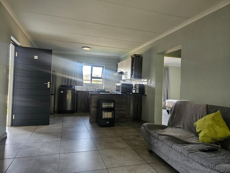 Open plan living area featuring tiled flooring and a functional kitchen with cabinetry, subway tile backsplash, and integrated extractor fan.