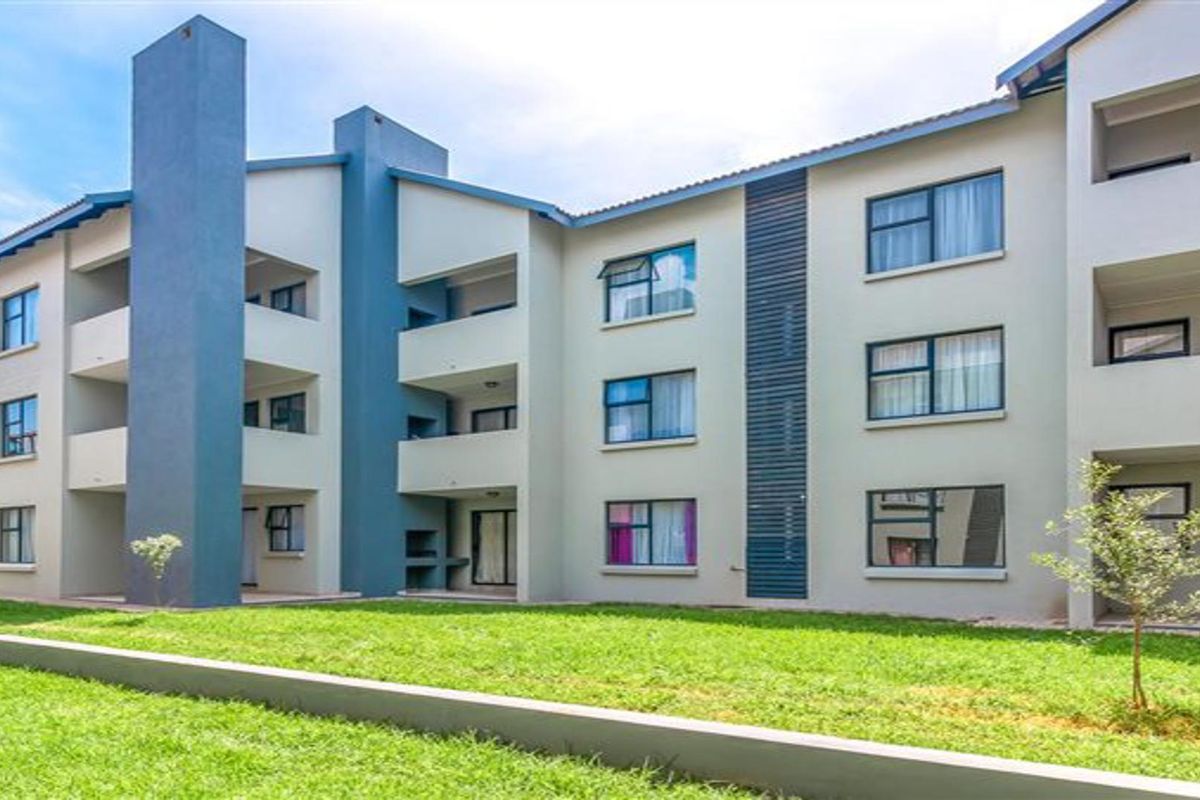 A view of the rear facade of a multi-story apartment complex featuring balconies, aluminium window frames, and a landscaped lawn area.