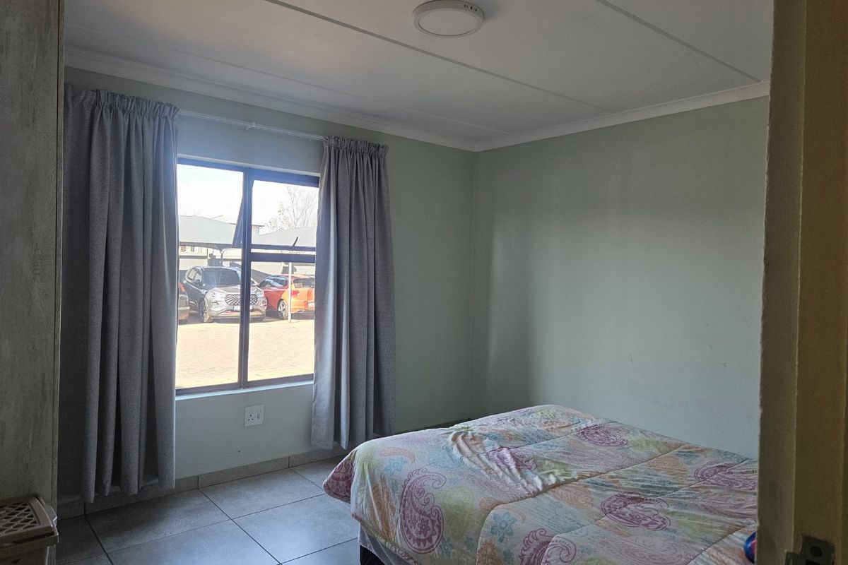 A functional bedroom featuring tiled flooring, neutral wall tones, and a large window allowing for natural light.