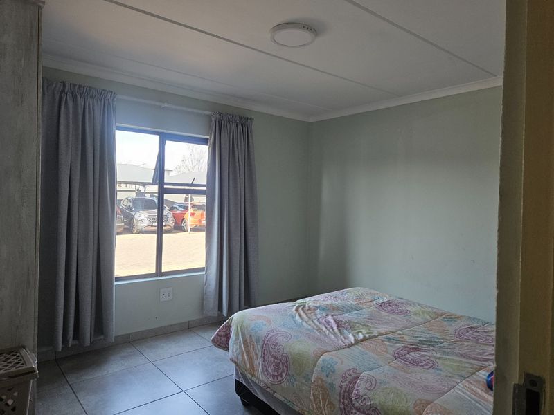 A functional bedroom featuring tiled flooring, neutral wall tones, and a large window allowing for natural light.