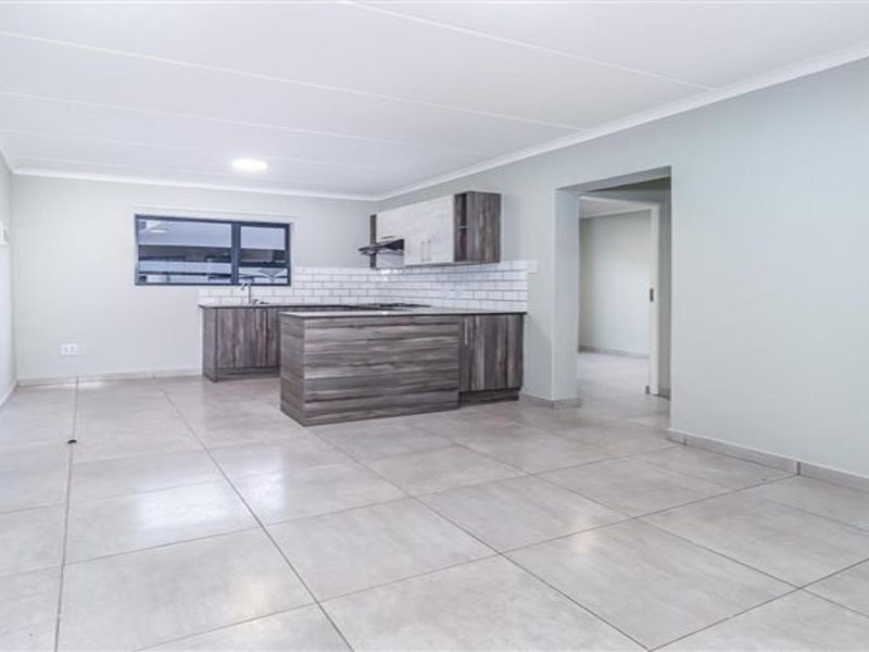 A bright, open-plan living and kitchen area featuring modern wood-finish cabinetry, a central island, subway tile backsplash, and neutral tiled flooring throughout.