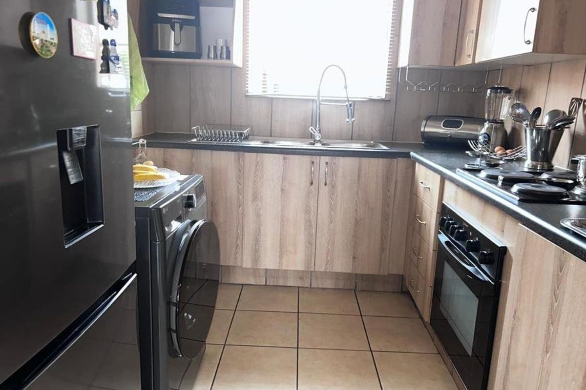 A functional kitchen featuring wood-look laminate cabinetry, dark countertops, a built-in oven with hob, and tiled flooring.