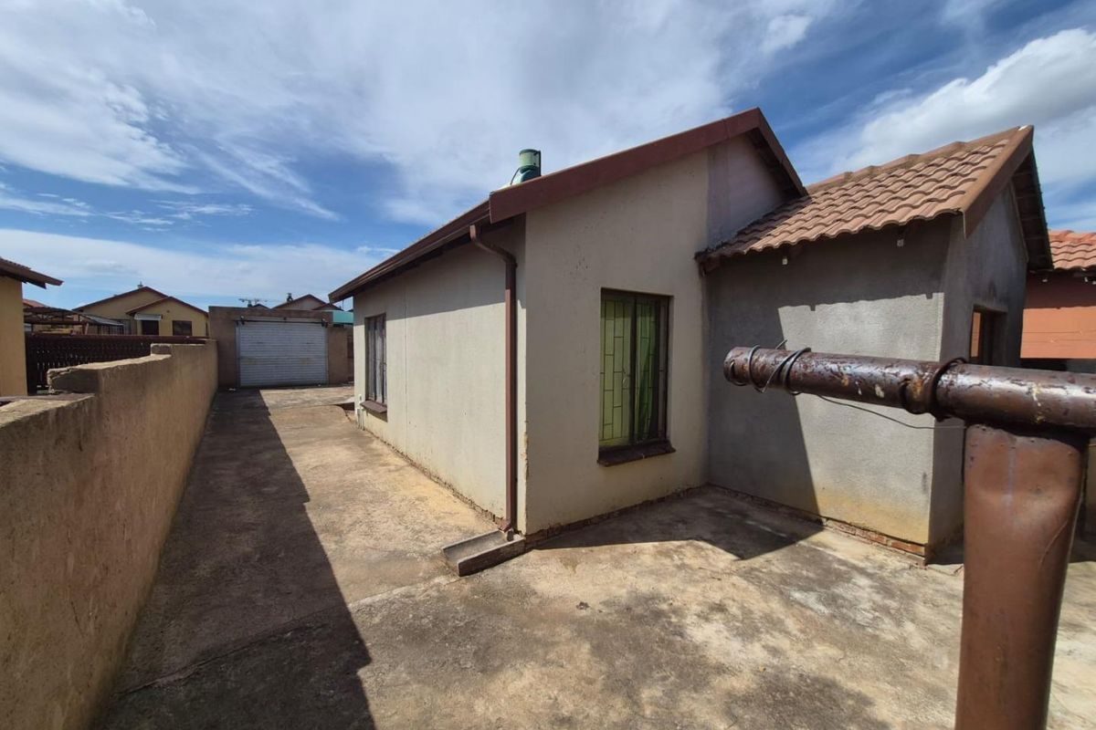 Rear exterior view of the property featuring a concrete driveway, perimeter wall, and detached garage with a tiled roof.