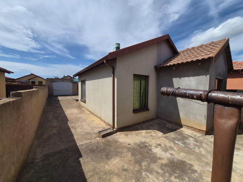 Rear exterior view of the property featuring a concrete driveway, perimeter wall, and detached garage with a tiled roof.