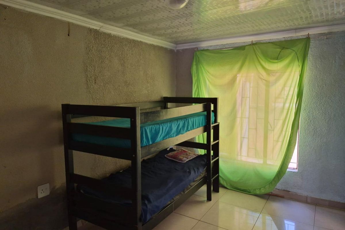 A bedroom featuring tiled flooring, textured walls, and security bars on the window, requiring cosmetic updates to improve the overall finish and aesthetic.
