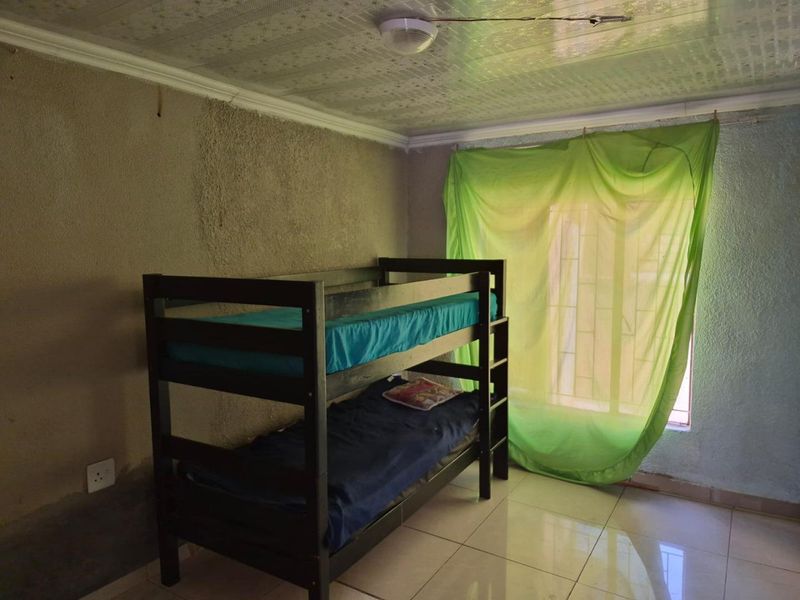 A bedroom featuring tiled flooring, textured walls, and security bars on the window, requiring cosmetic updates to improve the overall finish and aesthetic.