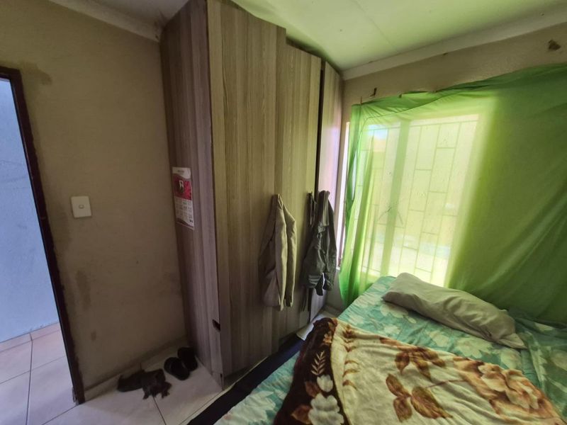 A bedroom featuring a built-in wardrobe, tiled flooring, and security bars on the window, currently showing signs of wear on the walls and ceiling.