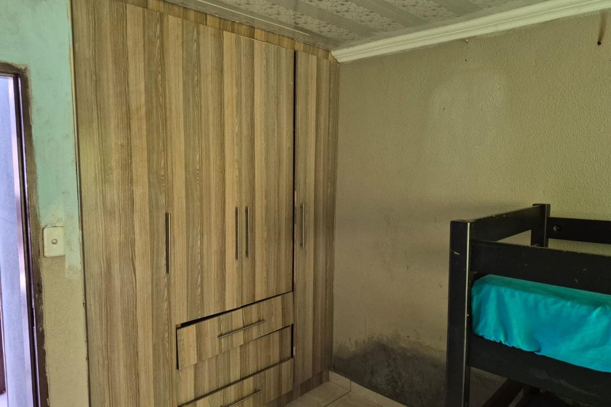 Bedroom featuring a built-in wooden wardrobe, tiled flooring, and visible wall dampness requiring maintenance and repair.