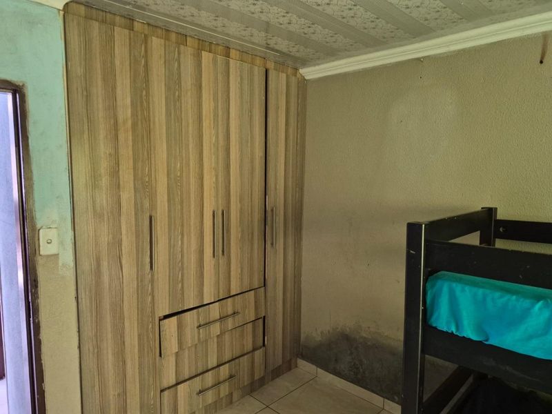Bedroom featuring a built-in wooden wardrobe, tiled flooring, and visible wall dampness requiring maintenance and repair.