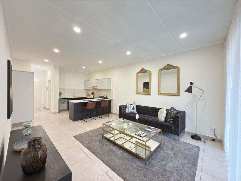 Modern open-plan living area featuring a sleek kitchen with island, recessed lighting, and neutral tiled flooring throughout.