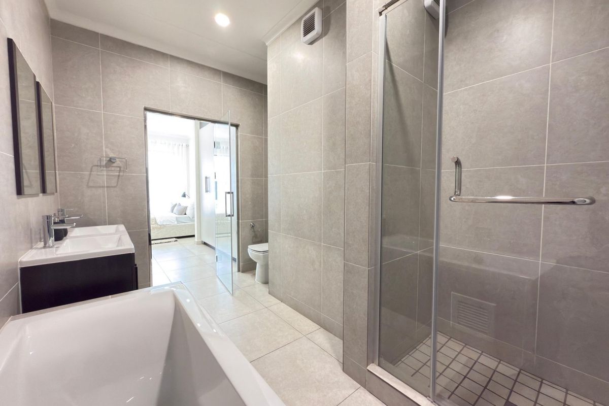 Modern bathroom featuring a double vanity, freestanding bathtub, and a separate glass-enclosed shower with neutral floor-to-ceiling tiling.