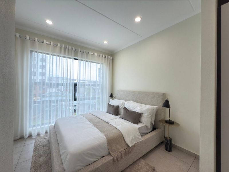 A well-lit bedroom featuring neutral tiled flooring, recessed ceiling lighting, and a large window providing natural light.