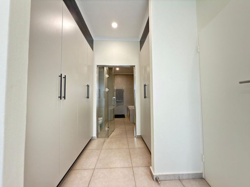 A clean, modern hallway featuring extensive built-in cabinetry, tiled flooring, and direct access to an adjoining bathroom through a glass door.