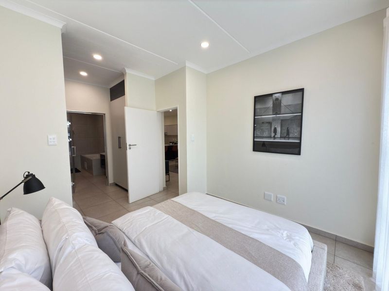 A well-maintained bedroom featuring tiled flooring, recessed downlighting, and convenient access to an en-suite bathroom with built-in storage.