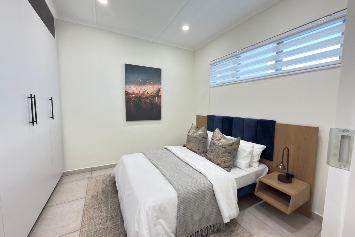 A modern, well-maintained bedroom featuring tiled flooring, built-in wardrobes, recessed lighting, and a horizontal window with fitted blinds.