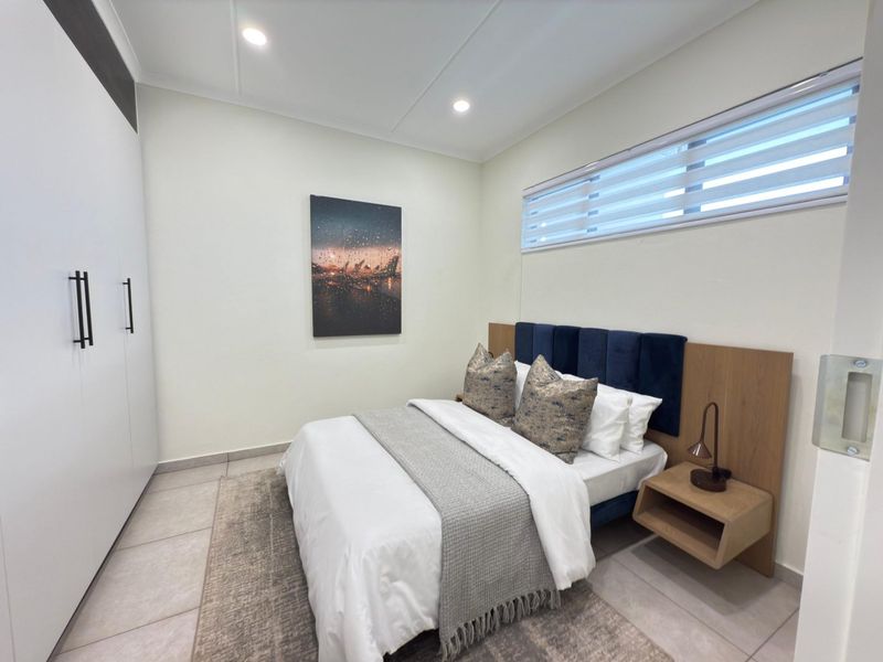 A modern, well-maintained bedroom featuring tiled flooring, built-in wardrobes, recessed lighting, and a horizontal window with fitted blinds.