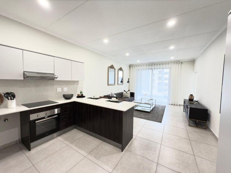 Modern open-plan apartment featuring a sleek kitchen with built-in appliances, stone countertops, and a spacious living area leading to a balcony.
