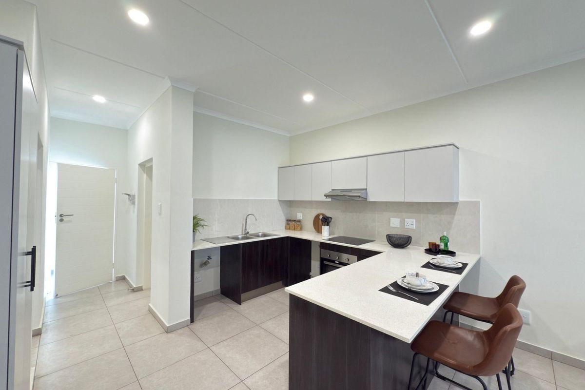 Modern kitchen featuring dark wood cabinetry, light stone countertops, integrated appliances, and a breakfast bar, finished with neutral floor tiles and recessed lighting.