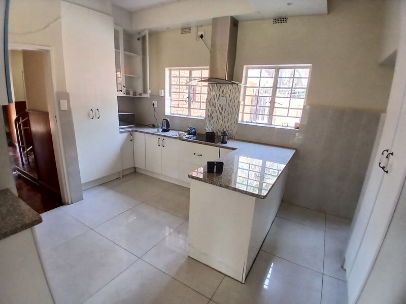 A functional kitchen featuring white built-in cabinetry, granite countertops, a central island, and a stainless steel extractor fan with tiled flooring.