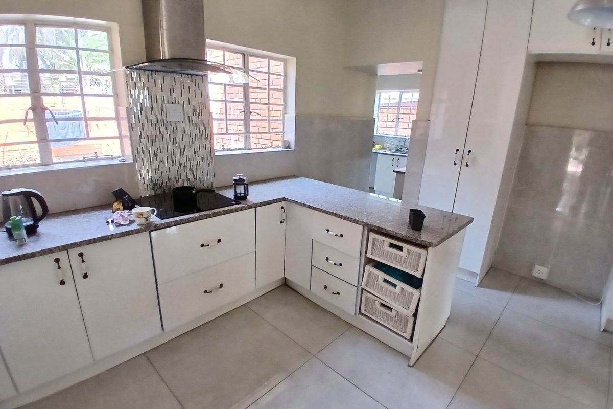 Modern kitchen featuring white cabinetry, granite countertops, a mosaic splashback, and a stainless steel extractor fan, with an adjacent scullery area.