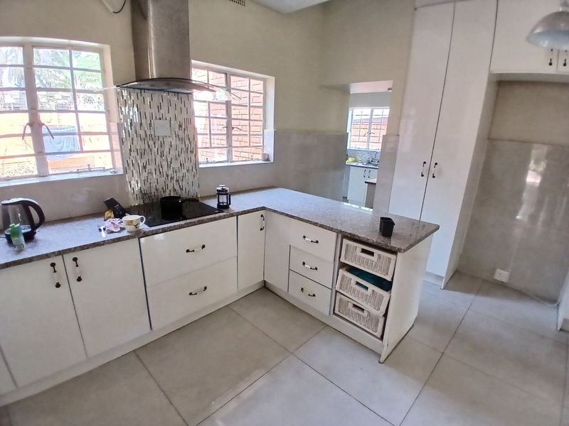 Modern kitchen featuring white cabinetry, granite countertops, a mosaic splashback, and a stainless steel extractor fan, with an adjacent scullery area.
