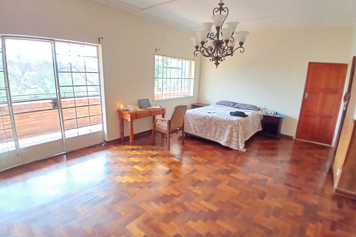 Spacious bedroom featuring classic parquet flooring, a decorative wrought iron chandelier, and direct access to an outdoor balcony through sliding glass doors.