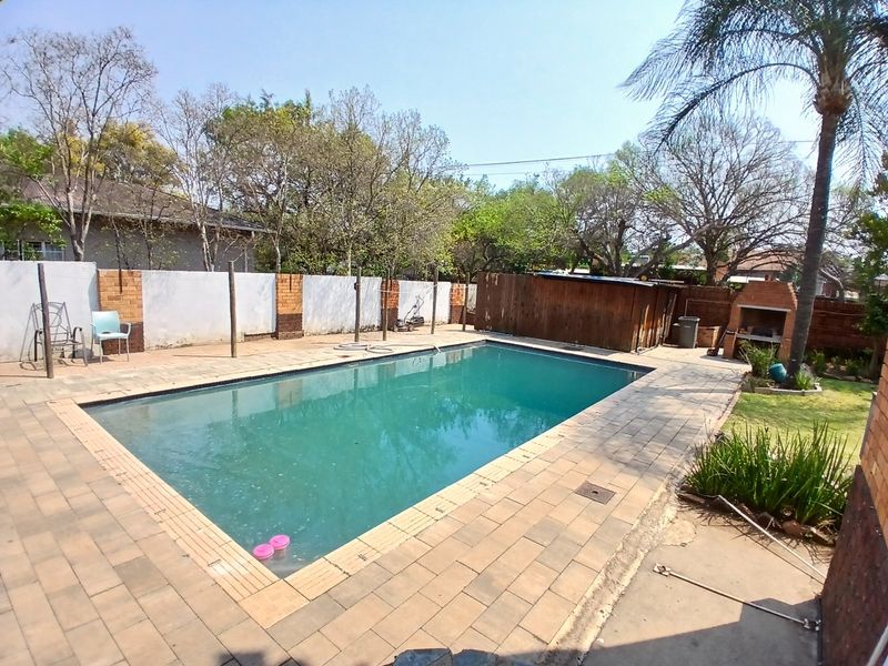 Outdoor pool area featuring a swimming pool, paved surround, and a built-in brick braai, set within a private garden with boundary walls.