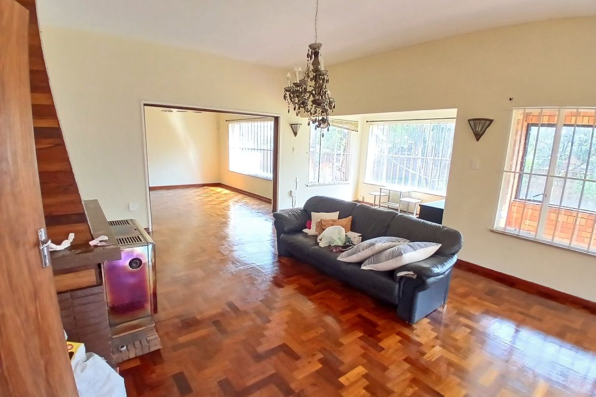 Spacious living room featuring classic parquet flooring, a built-in fireplace, and large windows with security bars, offering a bright and open living space.