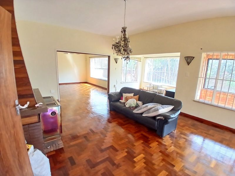 Spacious living room featuring classic parquet flooring, a built-in fireplace, and large windows with security bars, offering a bright and open living space.
