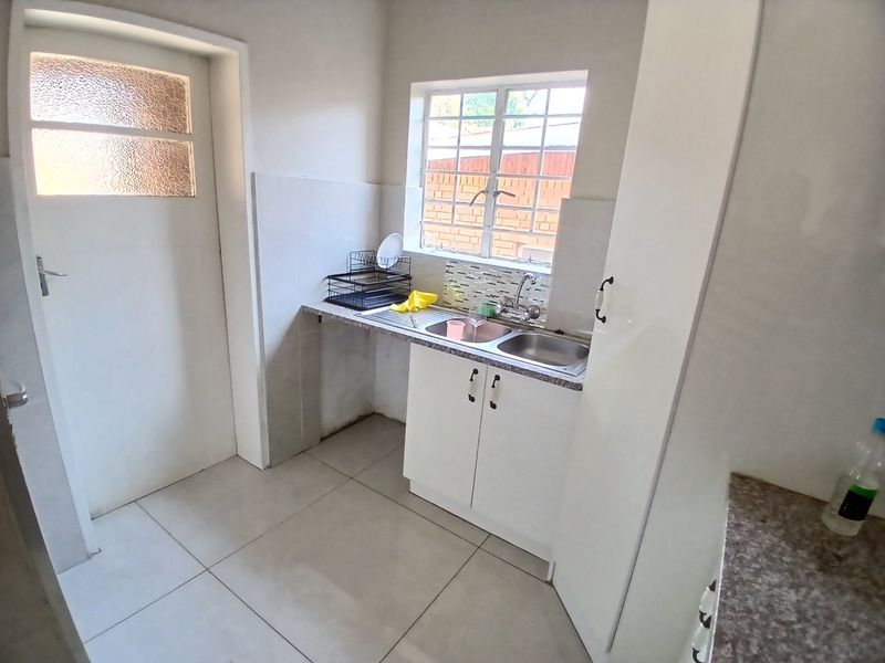 A functional scullery area featuring a double sink, built-in cabinetry, tiled splashback, and neutral floor tiles.