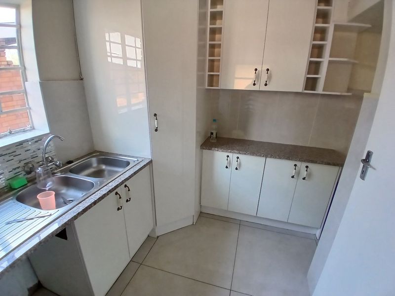 A clean and functional kitchen featuring white built-in cabinetry, double stainless steel sink, laminate countertops, and tiled flooring.
